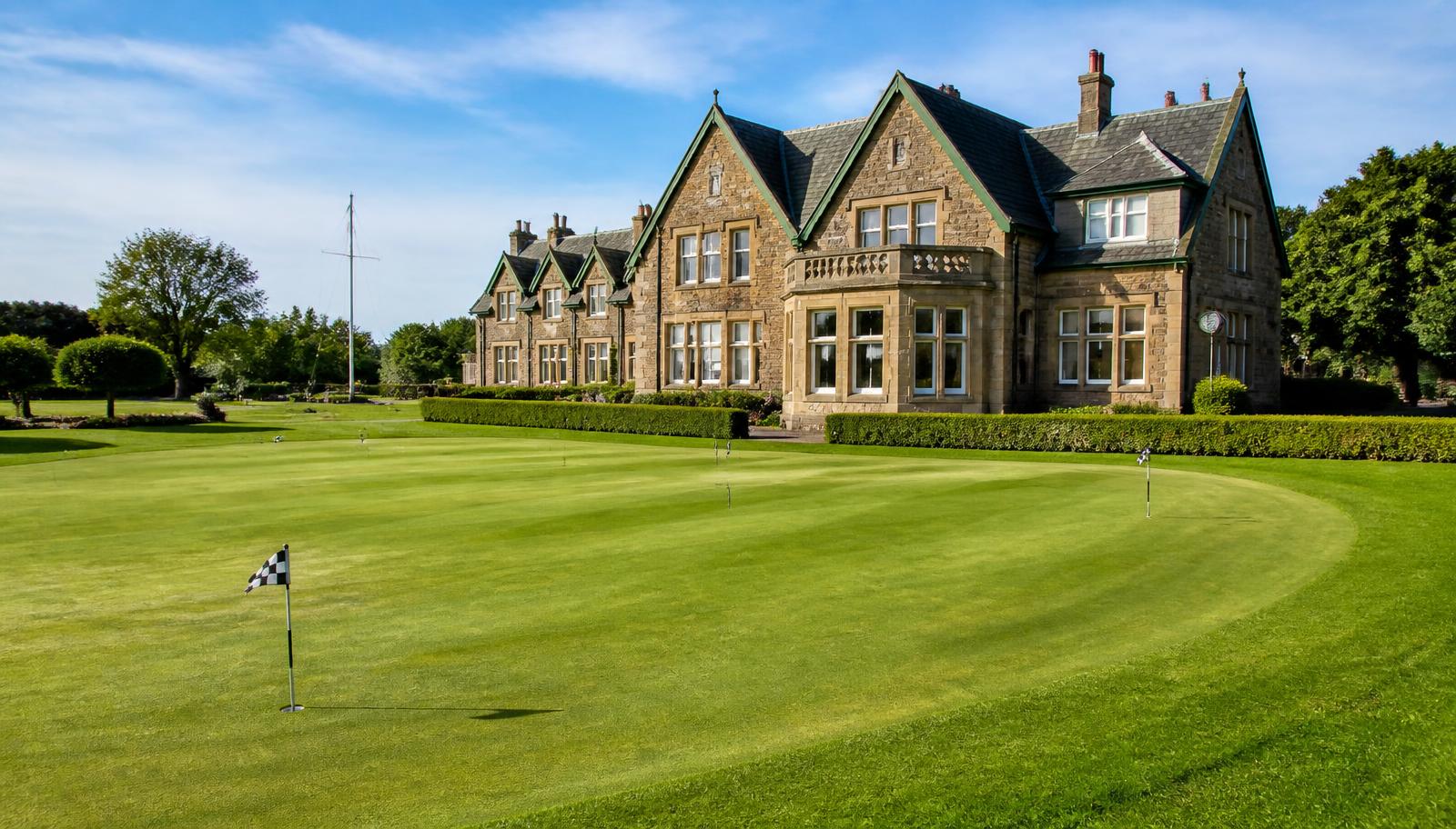 A golf club putting green in front of a traditional clubhouse