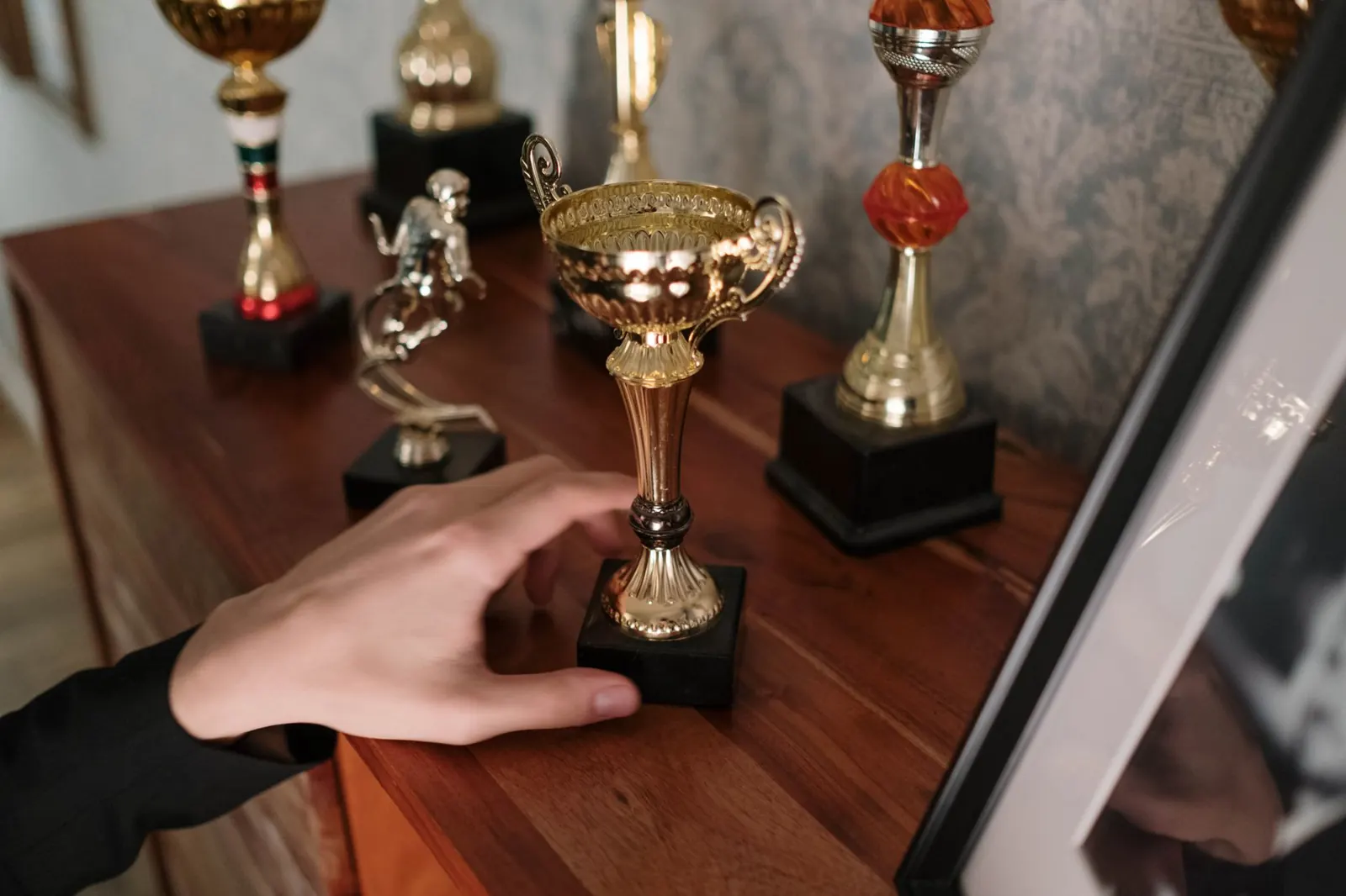 A row of trophies on a table with a hand lifting one of them