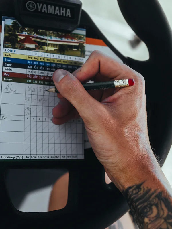 A player marking a scorecard with a pencil on a golf cart steering wheel