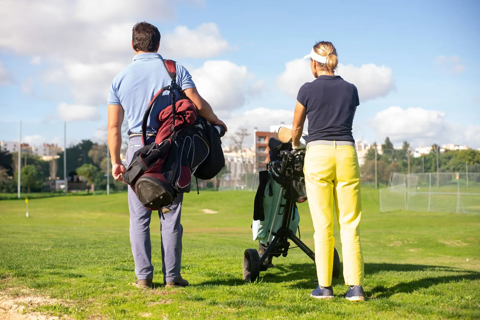 Two golfers carrying their bags walking across grass at a golf facility