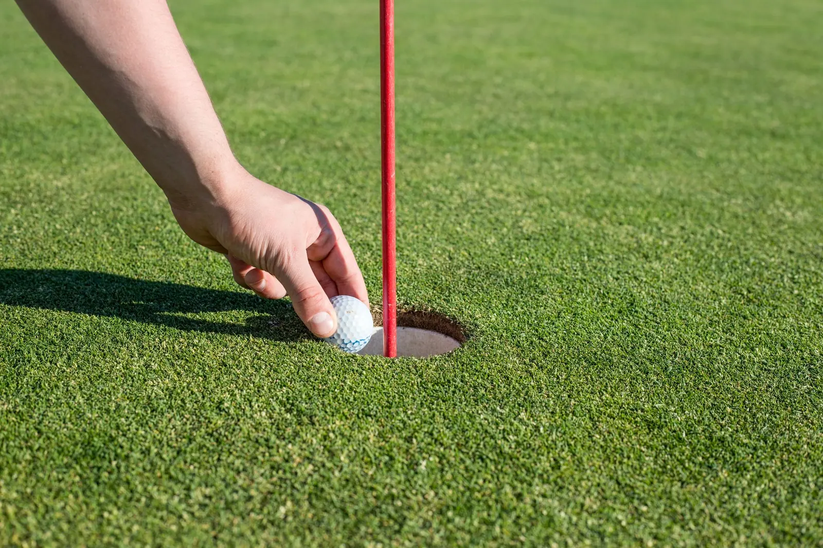 A golfer's hand placing a ball beside the hole on a putting green
