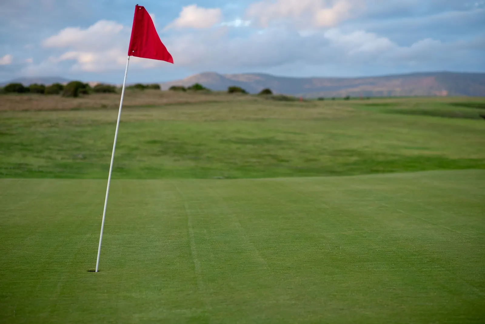 A red pin flag standing on a golf green with open countryside behind