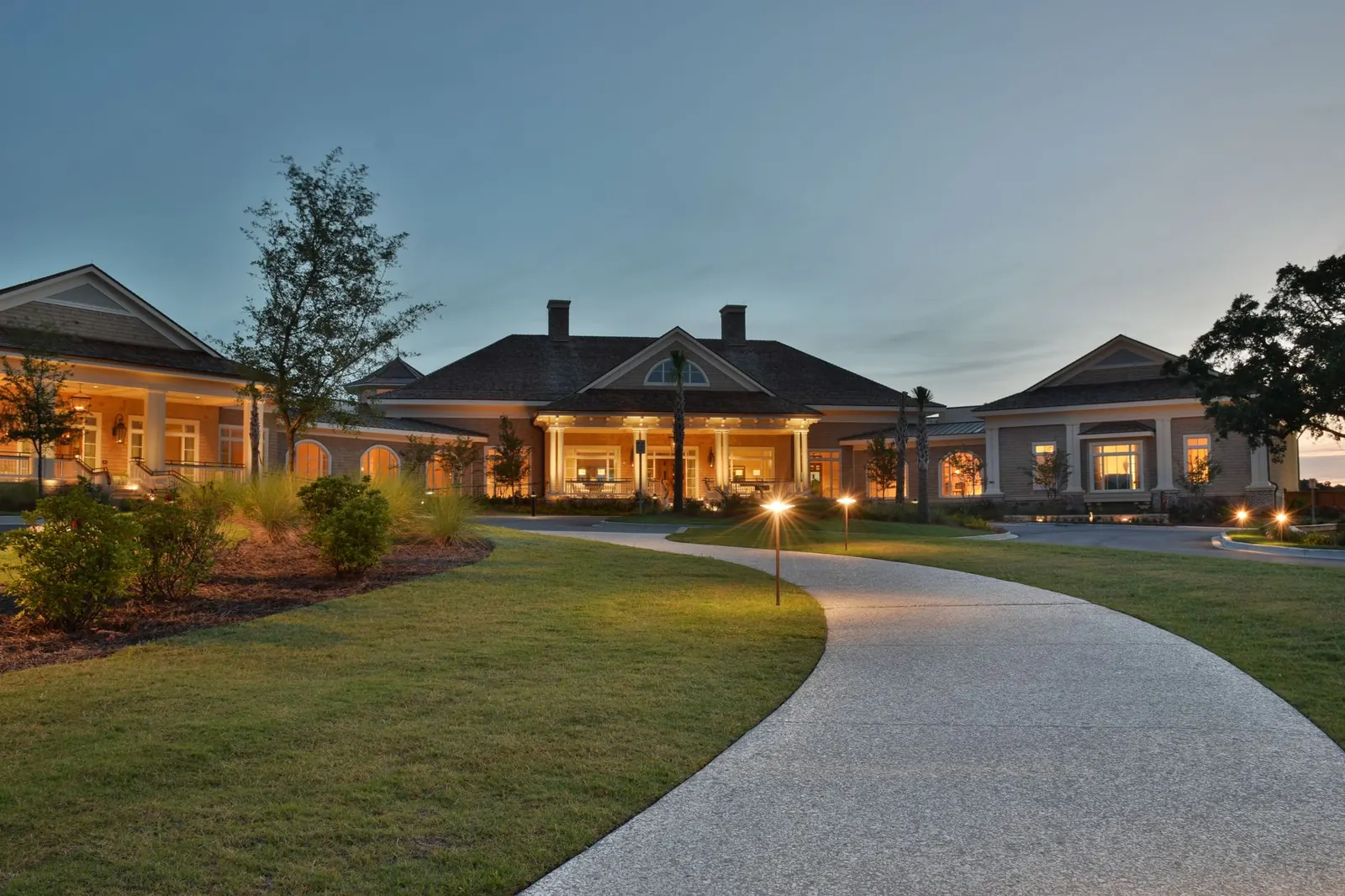 A golf clubhouse lit up at dusk at the end of a path