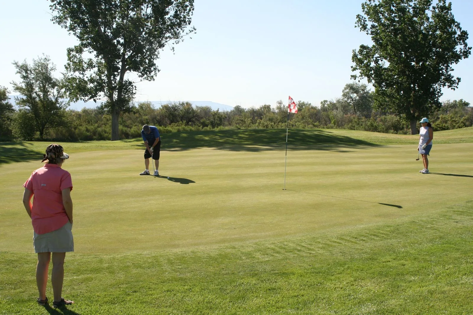 Three amateur golfers finishing a hole on a green beside the pin flag on a sunny day